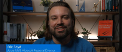 Un homme barbu est assis devant une bibliothèque.