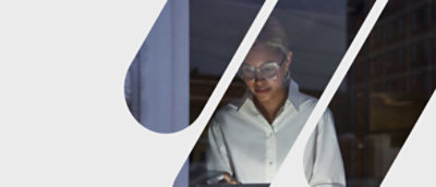 A woman wearing glasses and a white shirt works on a tablet at night, illuminated by the screen's glow and indoor lighting.