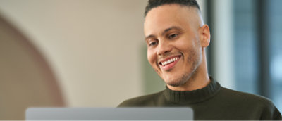 A man is smiling while using a laptop.