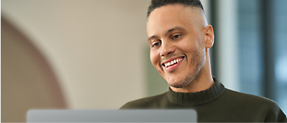 Un hombre sonríe mientras usa un portátil.