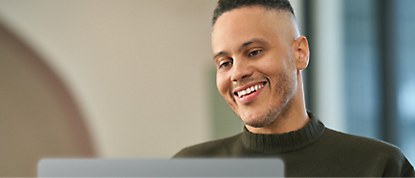 A man is smiling while using a laptop.
