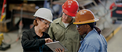 Three people in hard hats looking at a tablet.