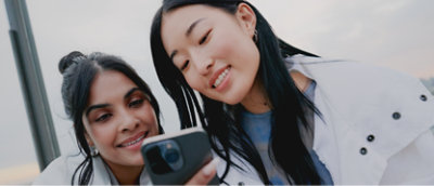 Two women are taking a selfie with their cell phones.