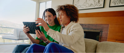 Two women sitting on a couch looking at a tablet computer.