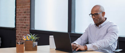 Un homme portant des lunettes et une t-shirt en train de travailler sur un ordinateur portable dans un environnement de bureau moderne.