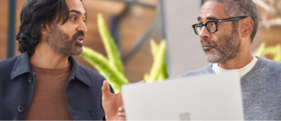 Ofis ortamında bir dizüstü bilgisayarın arkasında konuşmaya dalmış iki erkek.