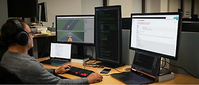 Um homem sentado a uma secretária com dois monitores e computadores portáteis