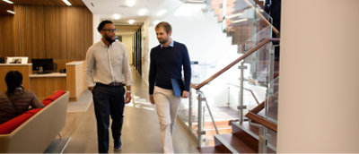 Deux hommes qui marchent et communiquent dans un bureau moderne.