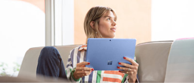 Femme tenant une tablette et regardant de façon réfléchie tout en étant assise sur un canapé.