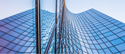 Gökyüzünü ve çevredeki binaları yansıtan eğri cepheli modern cam gökdelen.
