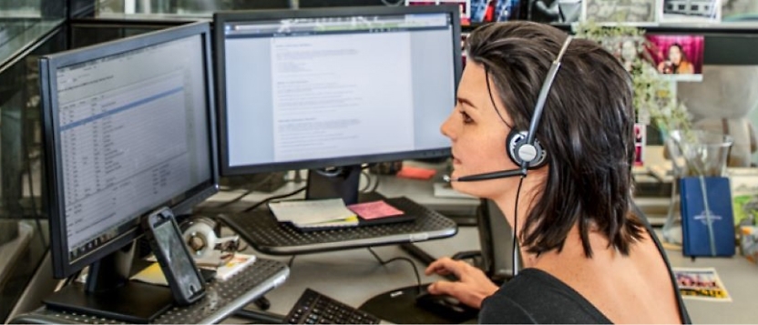 A woman wearing a headset and looking at the computer screen
