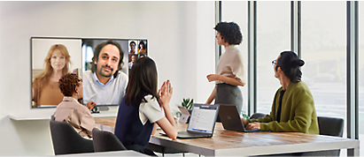 A group of people sitting at a table watching a video conference.