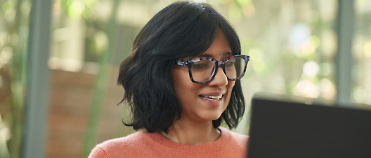 A smiling woman with glasses using a laptop.