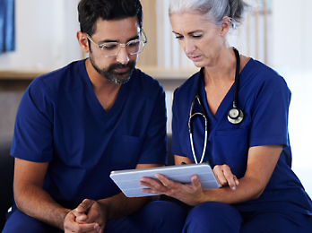 Een persoon en een individu die allebei een blauw ziekenhuisuniform dragen en naar een tablet kijken