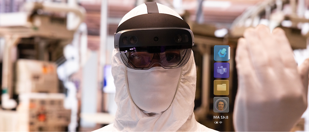 Eine Person in einem weißen Schutzanzug und einem Augmented Reality-Headset mit digitalen Symbolen, die vor ihr in der Luft schweben. 
