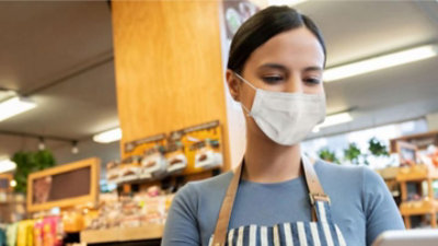 Eine Person mit Schürze und Maske, die auf ein Mobiltelefon blickt