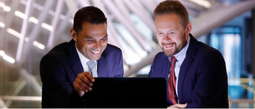Dos empresarios sonríen mientras miran un portátil.