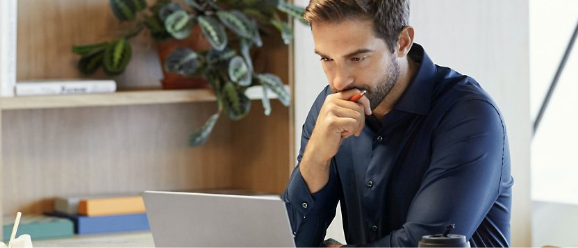 صورة رجل يجلس على مكتب وأمامه جهاز كمبيوتر محمول.