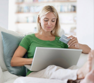 A smiling person holding a credit card while looking at her laptop computer.