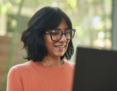 Person using laptop in a peach sweater with a soft green background.