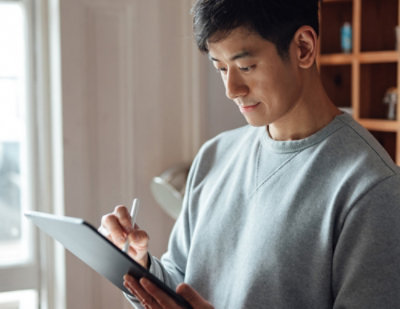 person writing on a tablet while standing near a window indoors