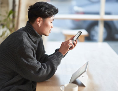 Person standing indoors holding smartphone near window in modern workspace