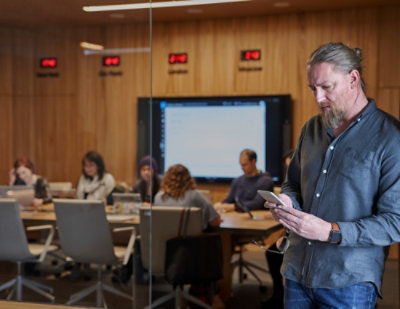 Man holding a tablet in a conference room with people working in the background.