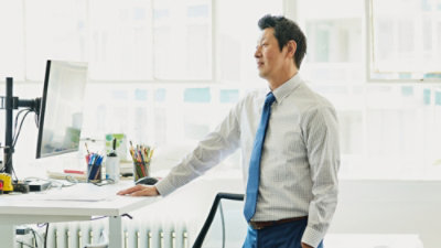 A man wearing a suit and tie stands next to a desk.