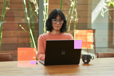 A woman wearing glasses sits at a table with a laptop.