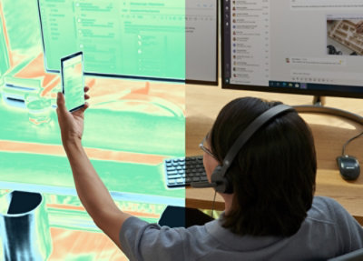  Person wearing headphones seated at a desk, holding a smartphone while working on two large monitors displaying applications and documents.