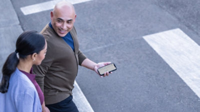 Two people walking outdoors while checking information on a smartphone.