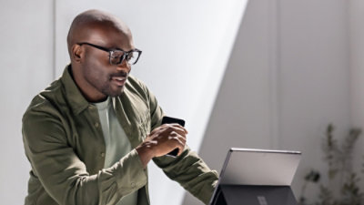 Person using a smartphone and laptop while standing in a bright indoor workspace.