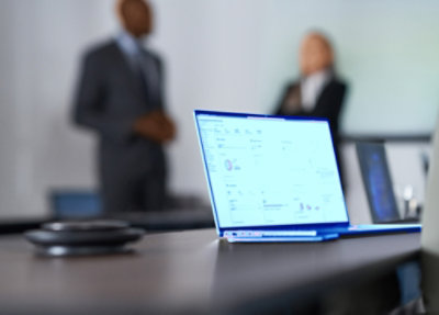 Laptop on a conference table with people in the background.