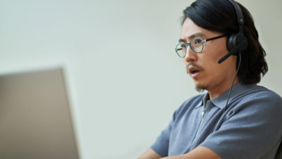 Person wearing headphones and working on a laptop in an indoor setting.