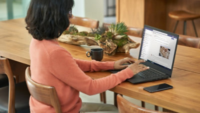 Working on a laptop at a wooden table with plants and a phone nearby