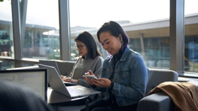 Woman using phone while working on laptop