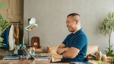 A man is smiling with his arms crossed while looking at a laptop.