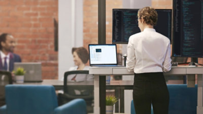Woman coding on laptop with external monitors