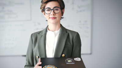 Person holding a laptop in front of a whiteboard.