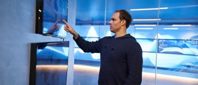 A man in a dark blue hoodie is interacting with a touchscreen display mounted on a wall.