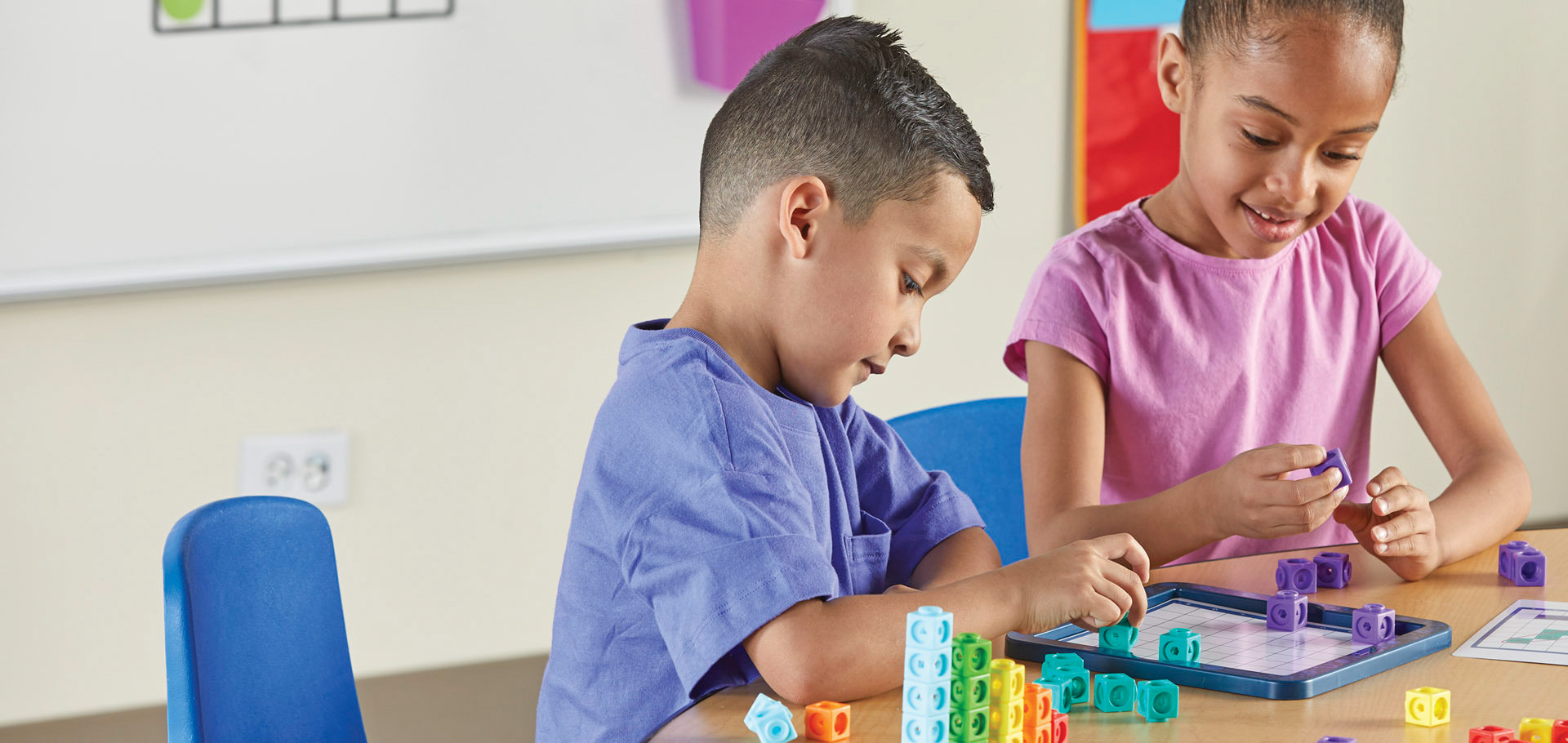 Two children are playing with colorful interlocking cubes and a tablet.