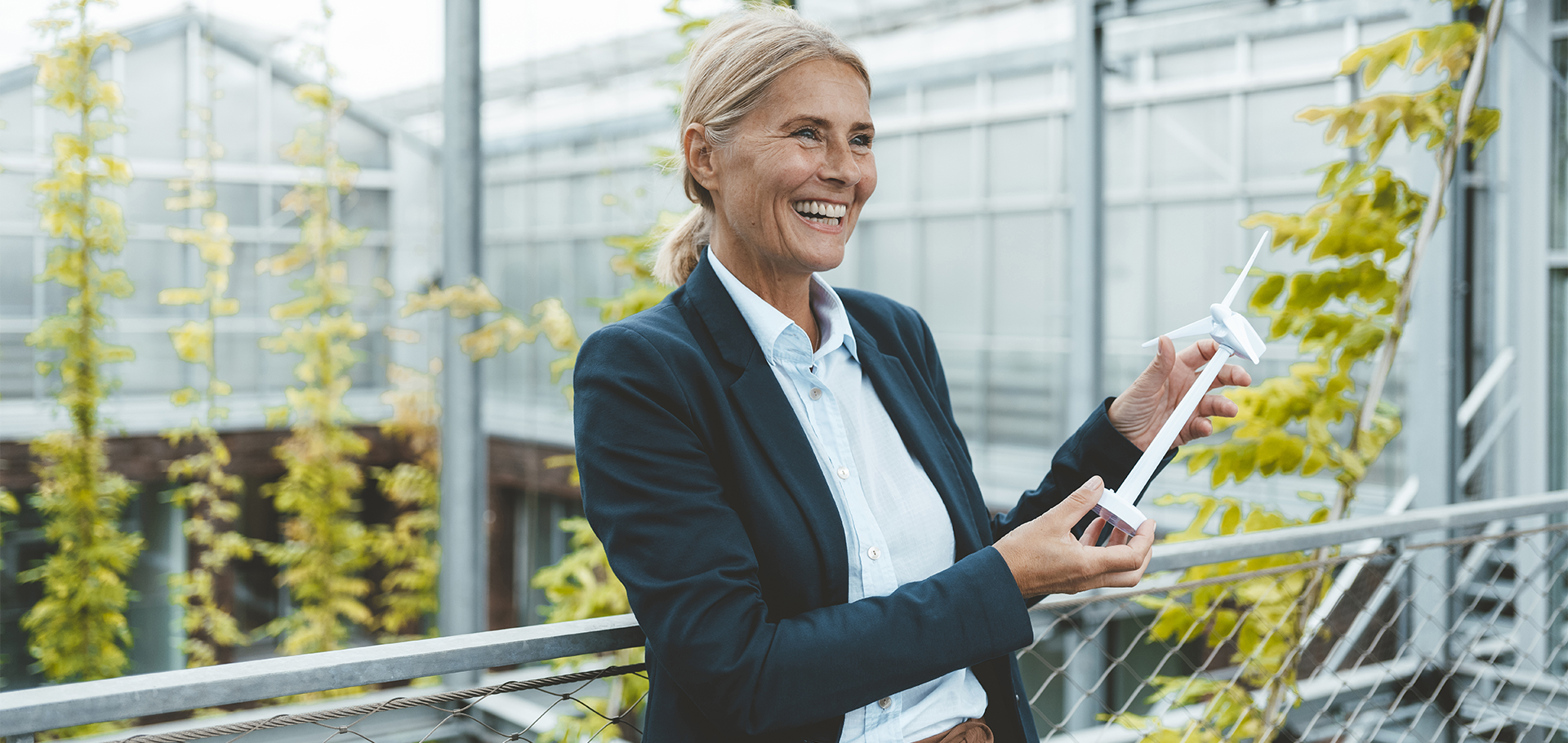 A person holding a caliper in an outdoor setting, likely near a greenhouse.