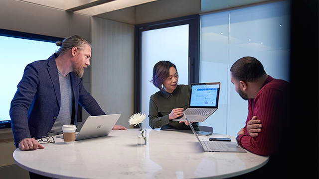 Two people are focused on a laptop screen displaying a website. The website features geometric graphics and a section with text. Both individuals are viewed from behind, suggesting collaboration or shared interest in the content. The setting appears to be a light-colored wooden table in an indoor environment, creating a casual and professional atmosphere.