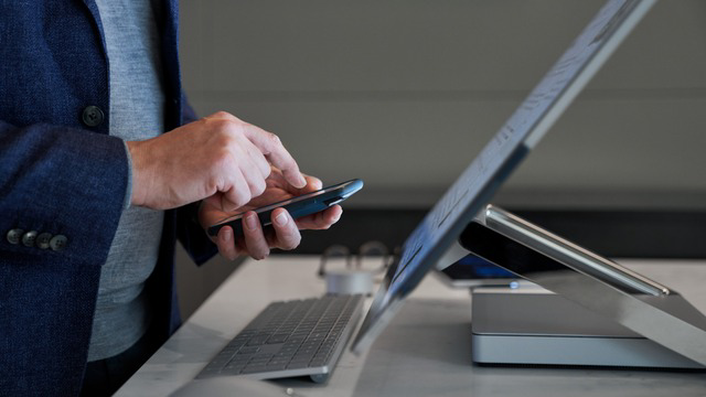 Professional using a smartphone while working on a laptop at a desk.