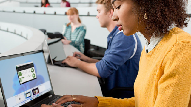 A woman attentively uses a laptop while seated in a lecture hall, surrounded by rows of empty seats.