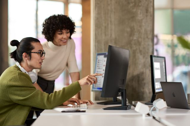 Two people collaborating at a desk while reviewing content on a computer screen.