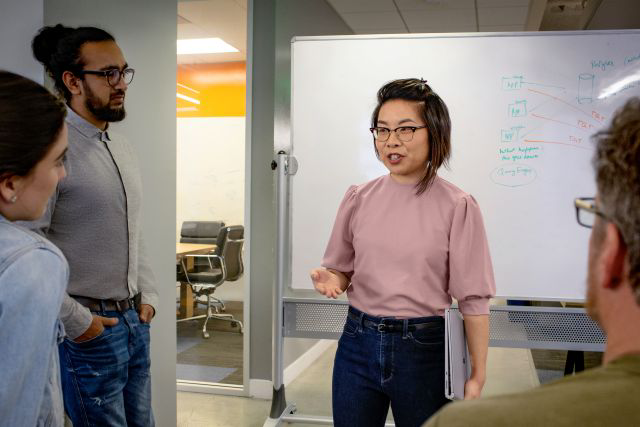 Colleagues standing together and discussing ideas in front of a whiteboard.