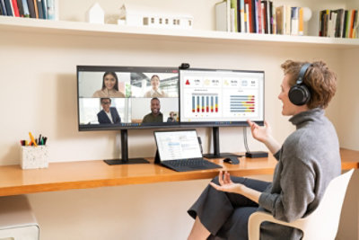 אדם עם אוזניות יושב ליד שולחן שעליו שני צגים; מסך אחד מציג שיחת ועידת בווידאו עם ארבעה משתתפים