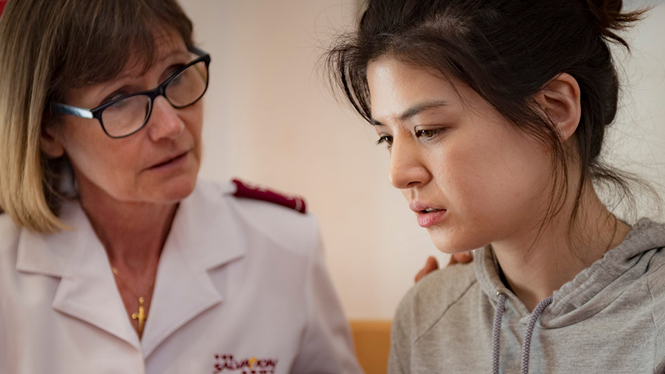 Person in a Salvation Army uniform sits beside another person with a hand resting on the shoulder in a supportive gesture.