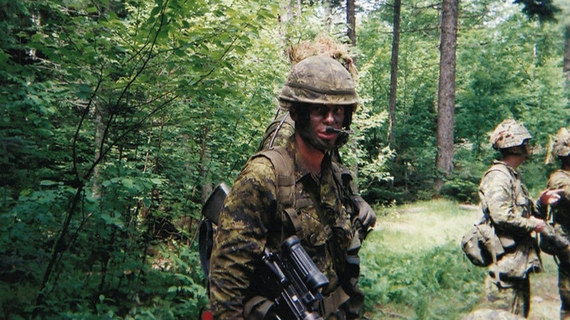 Scott Savage in military uniform camouflaged in a forest